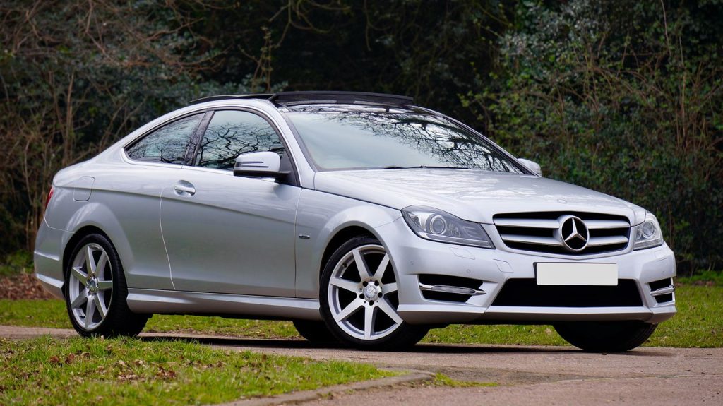 A sleek silver Mercedes-Benz coupe parked on a quiet, scenic road surrounded by greenery.