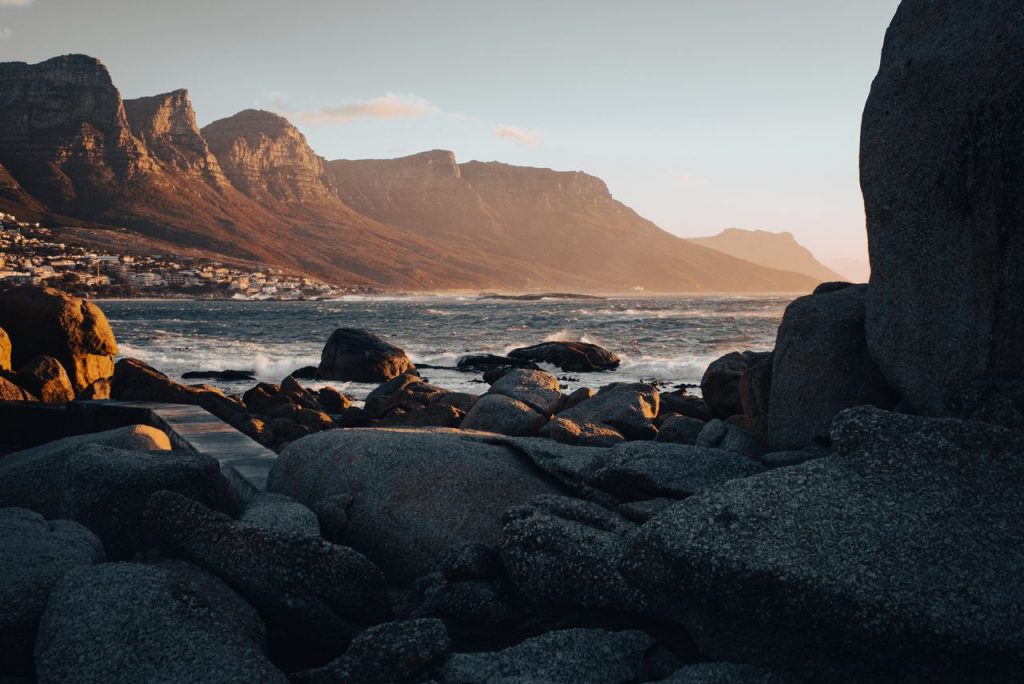 Stunning view of Cape Town's rocky coastline at sunset with mountains in the background.