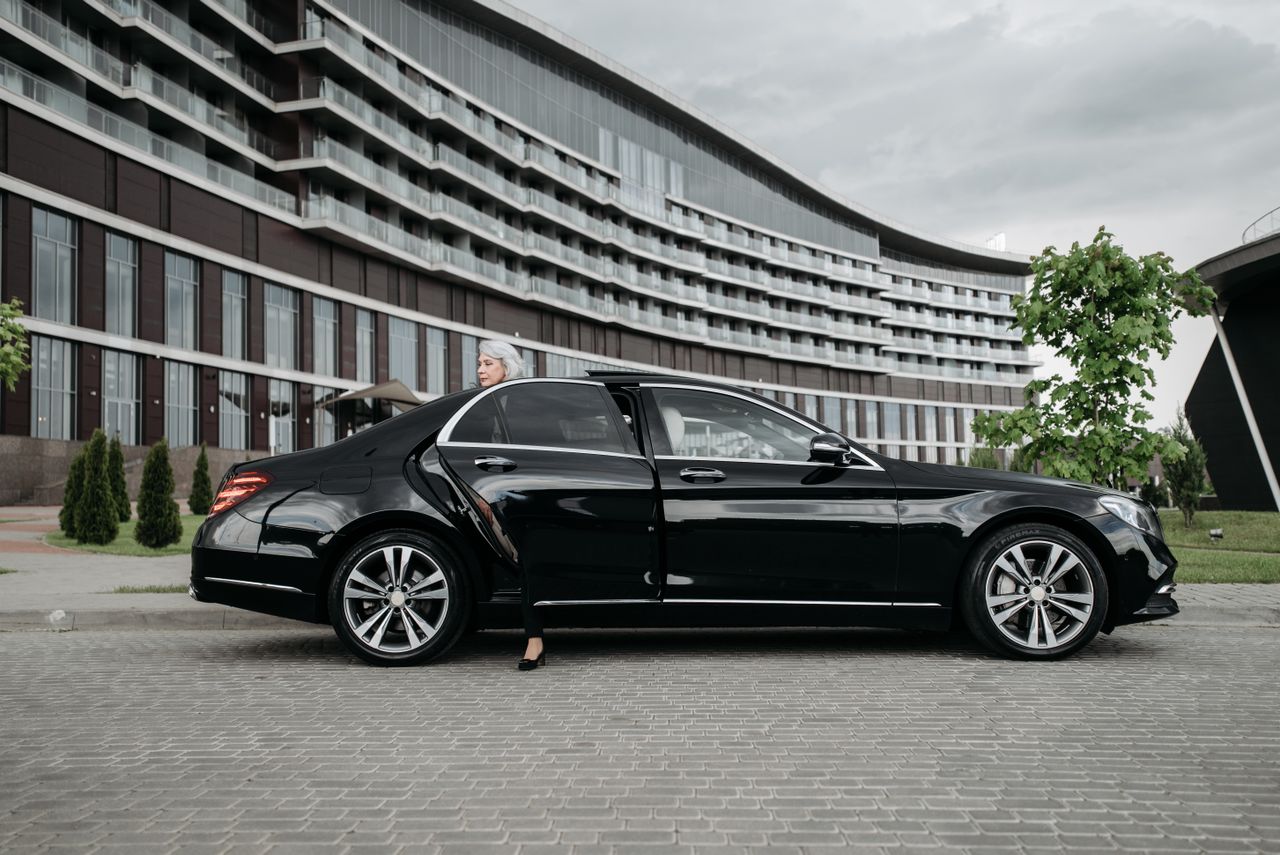 Senior businesswoman exiting a sleek black car in front of a modern building.